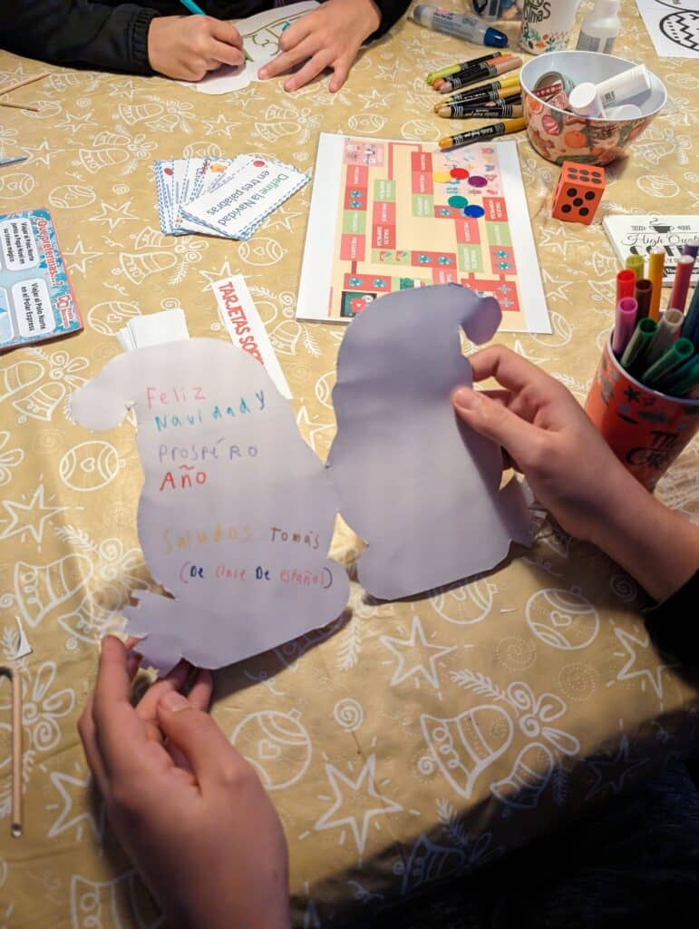 Kinderen maken Spaanse kerstkaarten tijdens een creatieve Spaanse lesactiviteit, omringd door spellen en knutselmateriaal.